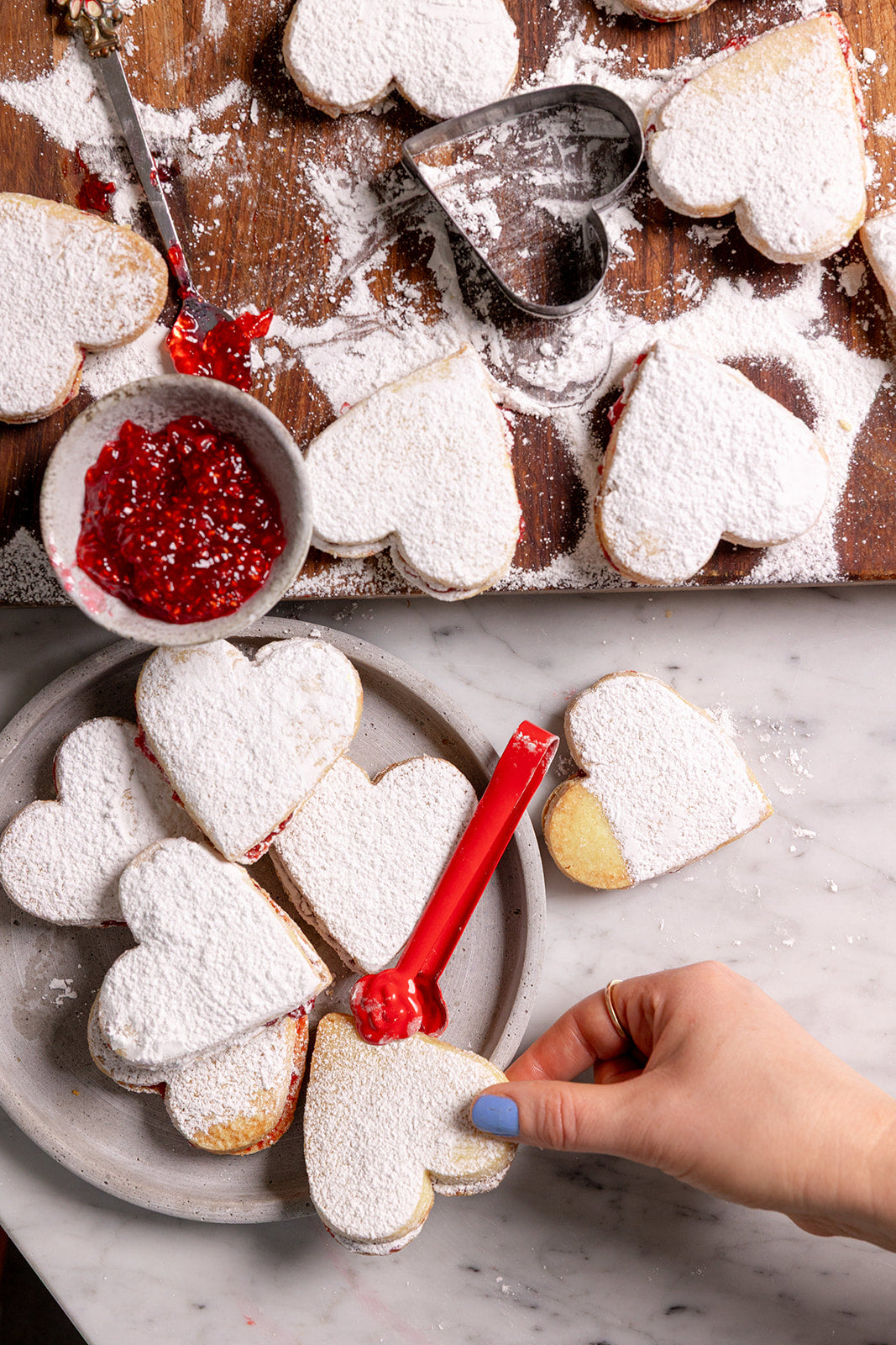 A hand lifting a vanilla shortbread heart with raspberry jam